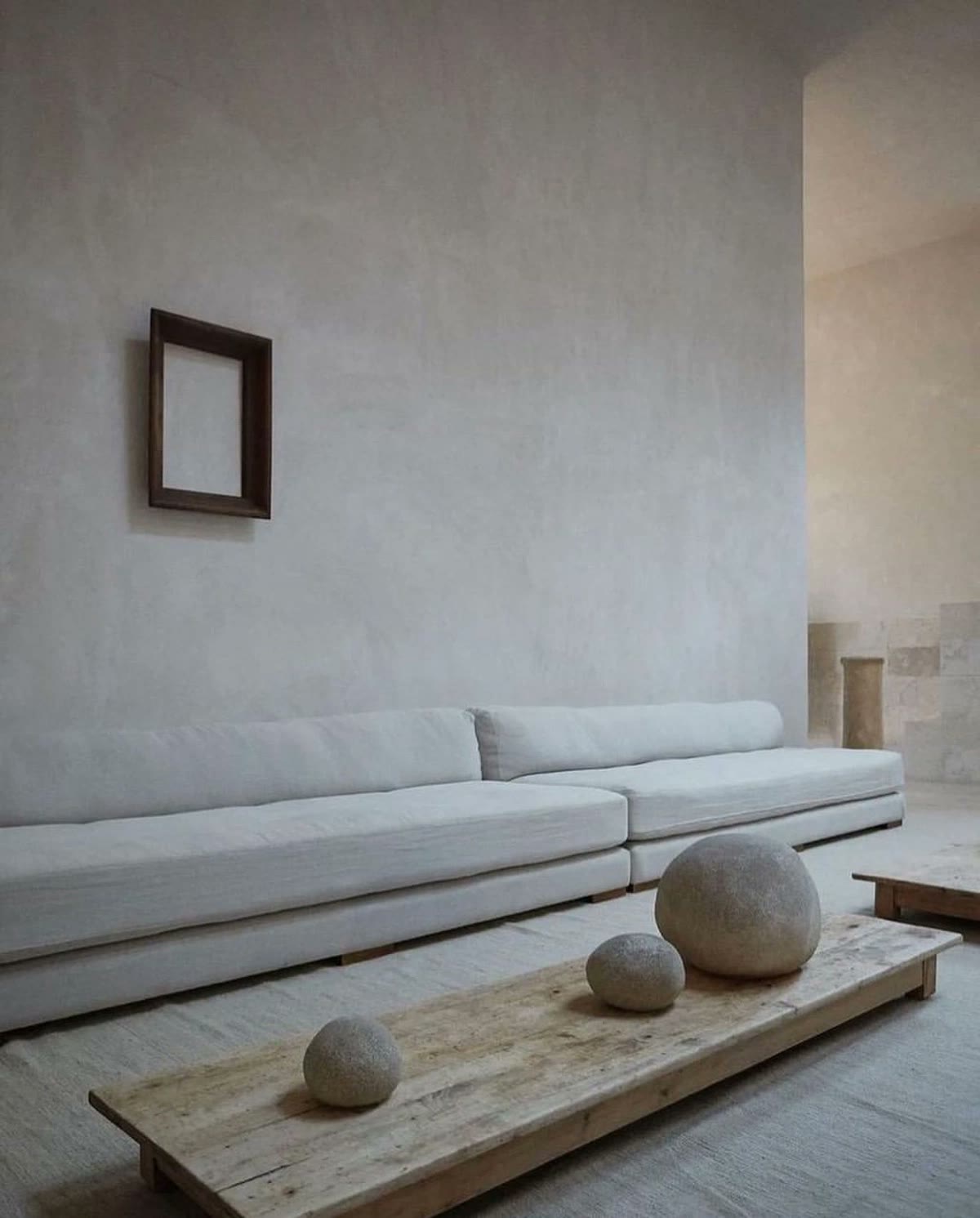 A plaster sitting room with a linen sofa and river stones on a wood bench