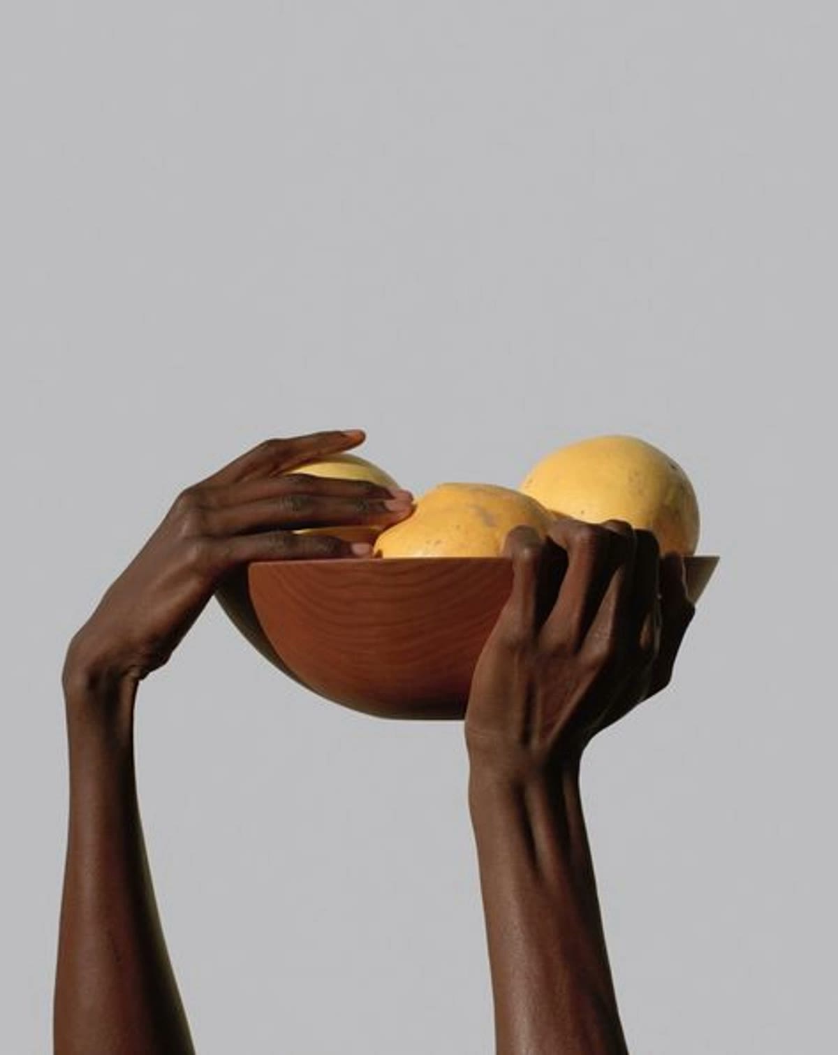 Hands lifting a wooden bowl of citrus